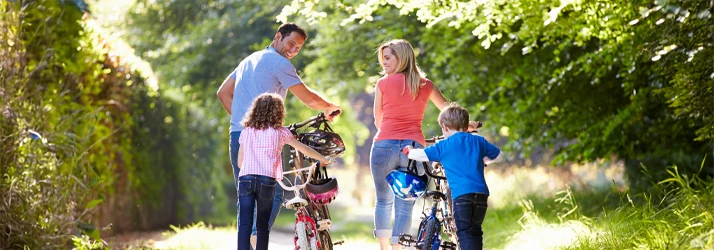 Four people standing with bicycles on a sunlit path surrounded by green trees and vegetation.