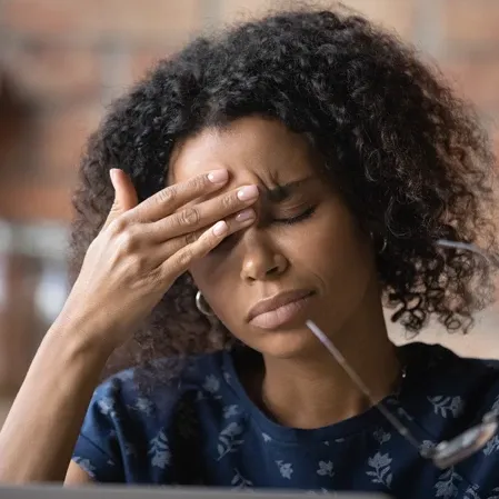 Close-up of a person touching the forehead with one hand while holding eyeglasses near the face.