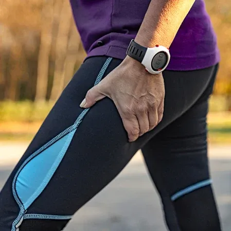 Close-up of a person holding the upper thigh while wearing black and blue athletic pants and a wristwatch.